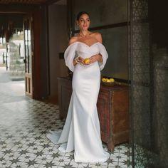 a woman in a white dress standing next to a wall holding a plate of fruit