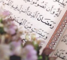 an open book with arabic writing on it and flowers in the foreground, against a white background