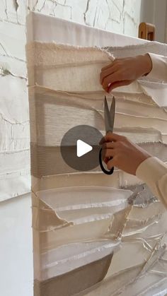 a woman is cutting fabric with scissors on a piece of cloth that has been taped to the wall