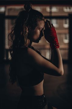 a woman wearing red boxing gloves and holding her hands up to her face in the dark