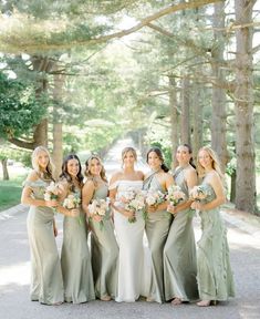 a group of women standing next to each other in front of trees and grass covered ground