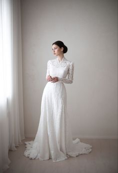 a woman in a white dress is standing near a window and looking off to the side