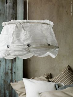 a white lamp hanging from the ceiling over a bed with pillows and blankets on it