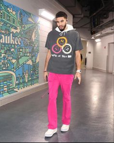 a man in pink pants and a black shirt is standing near a wall with a painting on it