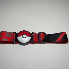 a red and black belt with a pokeball on the front, sitting on a white surface