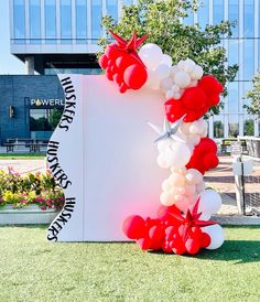 a large white sign with red and white balloons on it in front of a building