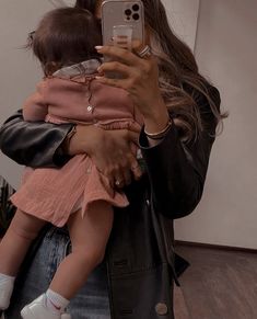 a woman taking a selfie with her cell phone while holding a baby in her arms