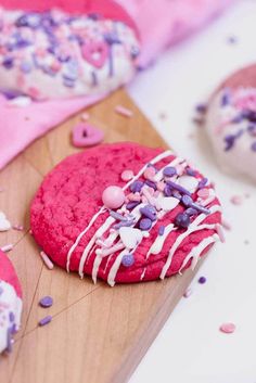 a pink cookie with sprinkles and white icing on a wooden cutting board