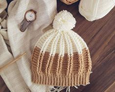 a white and brown knitted hat sitting on top of a table next to a watch