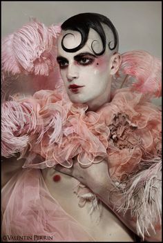 a man with white makeup and pink feathers on his face, wearing a costume made of feathered material