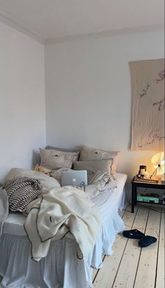 a bedroom with white walls and wooden flooring has a bed covered in blankets and pillows