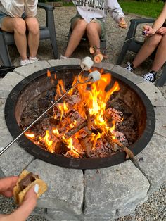 people sitting around an outdoor fire pit with marshmallows on the grill and hot dogs