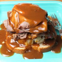 a blue plate topped with meat and gravy covered in sauce next to a fork