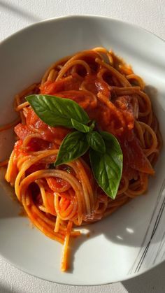 pasta with tomato sauce and basil leaves in a white bowl on top of a table