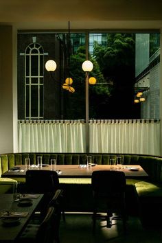 an empty restaurant with green velvet booths and long tables in front of large windows that have vertical blinds on them