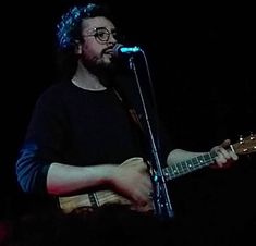 a man holding a guitar while standing in front of a microphone