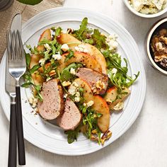 a white plate topped with meat and salad next to two bowls of food on top of a table