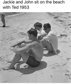 two men and a woman sitting on the beach with their arms around each other as they look at something