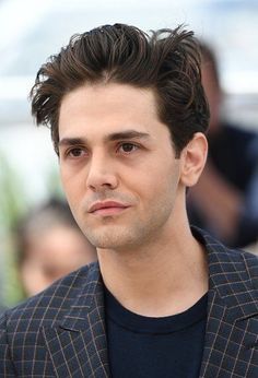 a close up of a person wearing a suit and black t - shirt with his hair pulled back