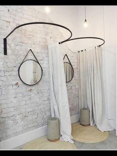 two round mirrors hanging on the wall next to a white brick wall with drapes