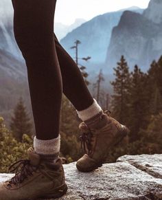 a person standing on top of a mountain with their legs crossed and wearing hiking boots