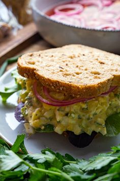 an egg salad sandwich with lettuce and radishes on a white plate