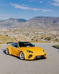 a yellow sports car parked on the side of a road with mountains in the background