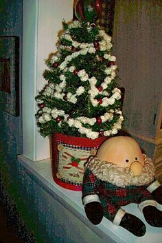 a stuffed animal is sitting on a window sill next to a christmas tree and potted plant