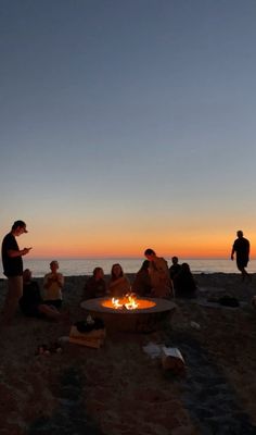 a group of people sitting around a fire pit on top of a beach next to the ocean