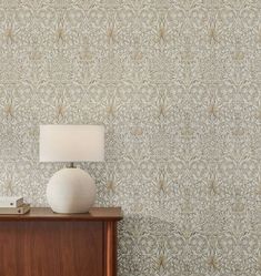 a white lamp sitting on top of a wooden table next to a wallpapered wall