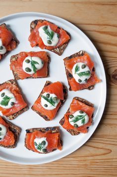 small pieces of bread topped with smoked salmon and cream cheese, on a white plate