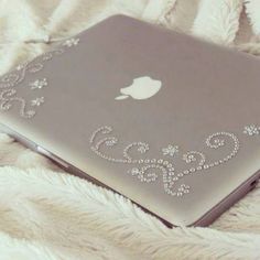 an apple laptop is sitting on a bed with white sheets and blankets behind it, decorated with swarongs