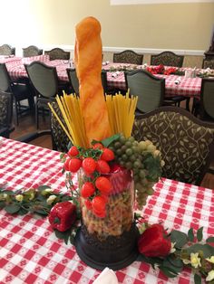 a table topped with a vase filled with food and veggies on top of it