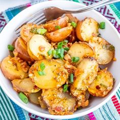 a white bowl filled with potatoes and green onions on top of a colorful table cloth