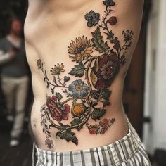 a man's lower back tattoo with flowers and leaves on the side, in front of his stomach