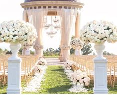 an outdoor ceremony setup with white flowers and chandeliers on either side of the aisle