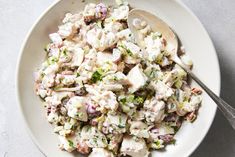 a white bowl filled with chicken salad on top of a gray countertop next to a silver spoon