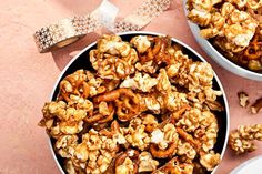 two white bowls filled with caramel popcorn on top of a pink tablecloth and ribbon