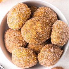 a bowl filled with sugared donuts on top of a white tablecloth next to an orange and black checkered napkin