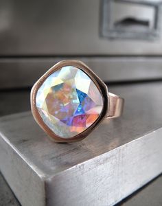 Romantic, other-worldly color... This dazzling Swarovski crystal cocktail ring has a 'Crystal AB' cushion-cut square stone... forever-sparkling crystal with soft, pastel flashes of every color in the rainbow, with a sheer, shimmering iridescent finish. The perfectly-faceted Swarovski cushion-cut crystal is set into a beautiful, high-quality, shiny light rose gold plated adjustable ring with an elegant, modern square bezel. Cushion-cut Swarovski crystal: 12mm dia (1/2") Shiny soft rose-gold plate Elegant Iridescent Rings For Parties, Elegant Iridescent Crystal Ring Adjustable, Elegant Iridescent Adjustable Crystal Ring, Elegant Crystal Jewelry, Swarovski Crystal Rings, Other World, Square Stone, Light Rose, Soft Rose