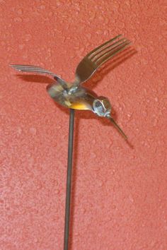 a small bird is perched on top of a metal pole with a fork in it's mouth