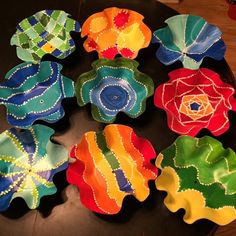 many different colored flower shaped dishes on a black table with wood flooring in the background