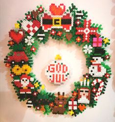 a christmas ornament made out of legos on a white wall next to a wreath with santa's sleigh, snowmen and other holiday items