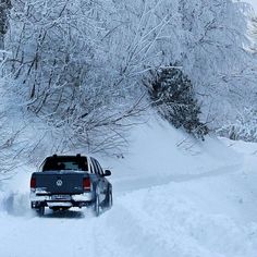 a car driving down a snow covered road next to trees and bushes on a snowy day