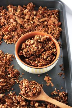 a bowl filled with granola sitting on top of a baking pan next to a wooden spoon