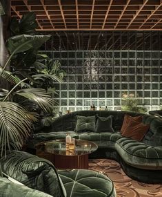 a living room filled with green couches next to a tall glass block wall covered in greenery