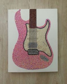 a pink and white guitar with lots of beads on it's body, sitting on top of a wooden surface