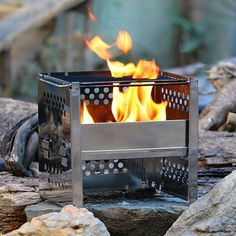 a metal fire pit sitting on top of a pile of rocks next to a forest