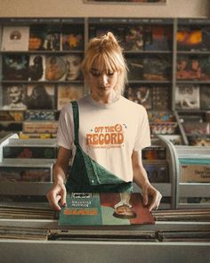 a woman standing in front of a record player holding an album and looking at it