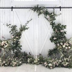 an arrangement of flowers and greenery arranged in front of a white wall with wooden doors